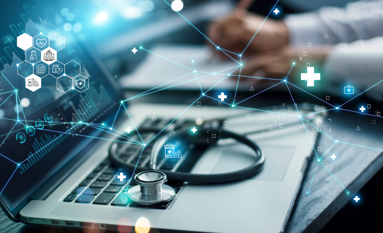 A laptop with medical icons displayed on the screen, alongside a stethoscope lying on the keyboard. A person's hands are writing notes in the background, suggesting a focus on digital healthcare.