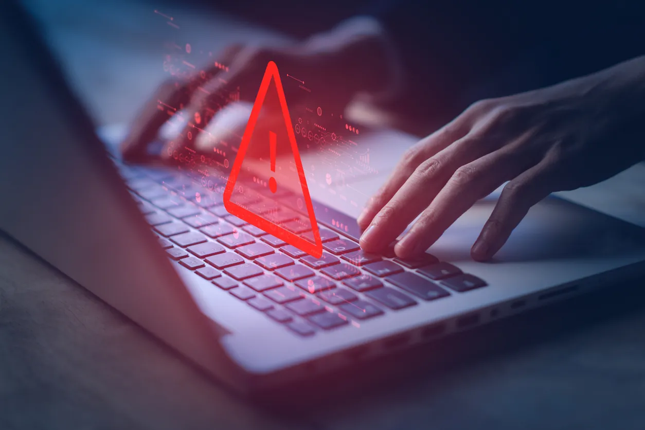 Close-up of hands typing on a laptop keyboard with a digital red warning icon overlay, indicating a potential security alert or issue.
